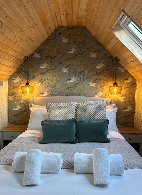 Cozy bedroom with wooden ceiling, patterned headboard, white pillows and teal cushions