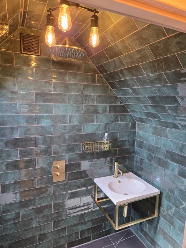 Modern bathroom with slate tile walls, white pedestal sink, brass fixtures and pendant lighting