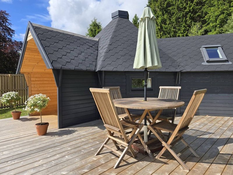 Exterior patio area with wooden dining table, chairs, umbrella and potted plants