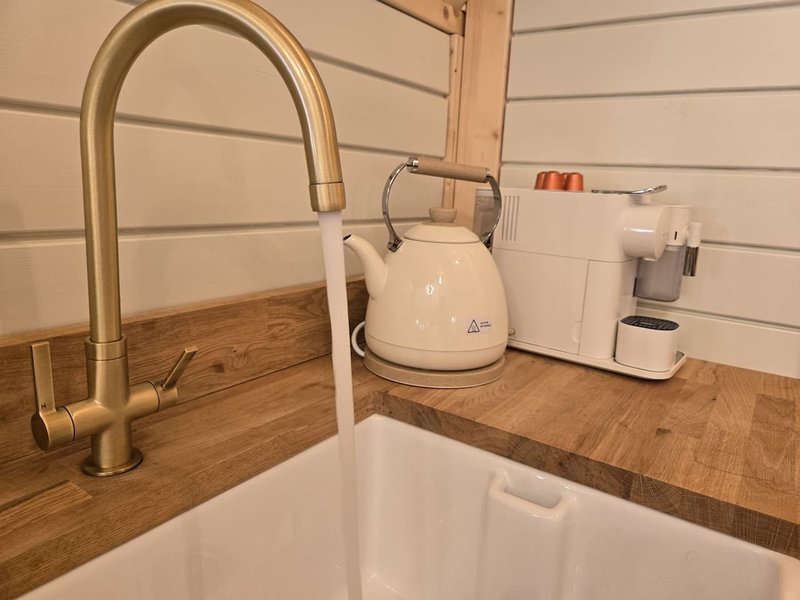 Kitchen sink with brass tap, wooden countertop, and white kettle and appliances