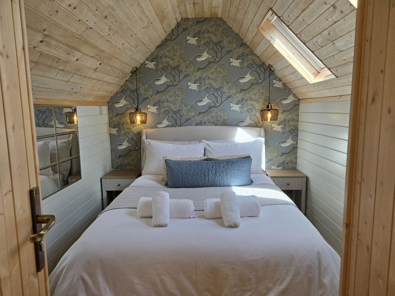 Cozy attic bedroom with double bed, patterned headboard wallpaper, wooden beams and skylight