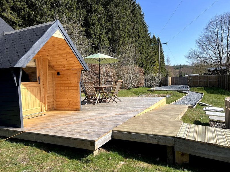 Wooden garden cabin with deck, patio furniture, umbrella and treeline backdrop