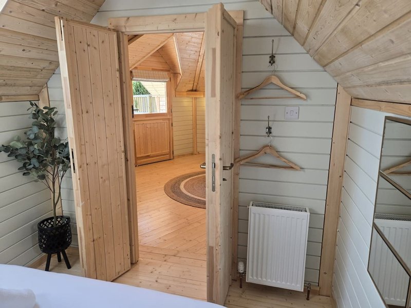 Wooden interior of glamping pod with open doors, wooden flooring and radiator visible