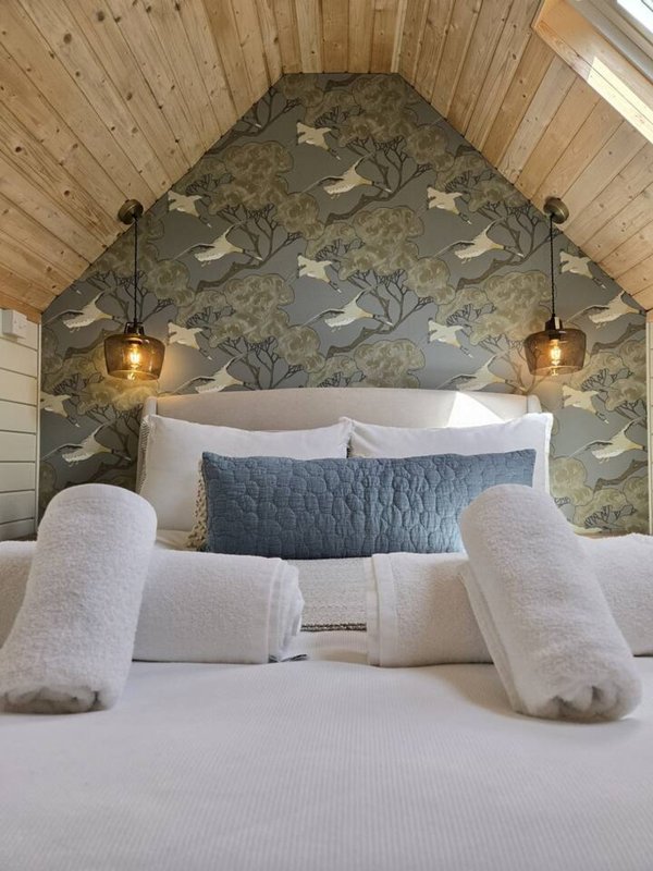 Bedroom with double bed, rolled towels, patterned headboard wall and pendant lights