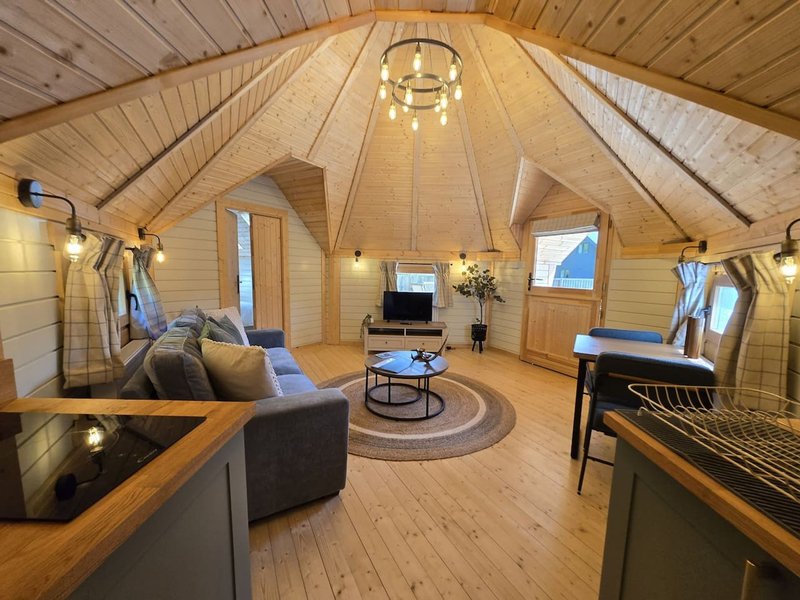 Open-plan interior of A-frame cabin with vaulted wooden ceiling, sofa, kitchen counter, piano, and windows