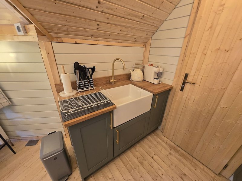 Compact kitchenette with cream sink, wooden countertop, dark cabinetry and wooden walls