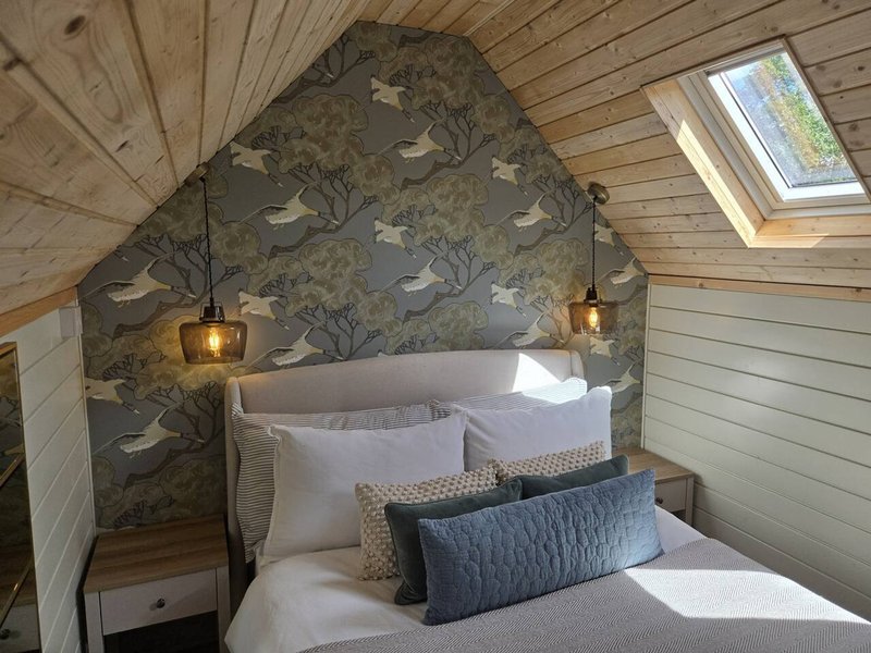 Cozy attic bedroom with patterned headboard, white bedding, decorative pillows and hanging pendant lights