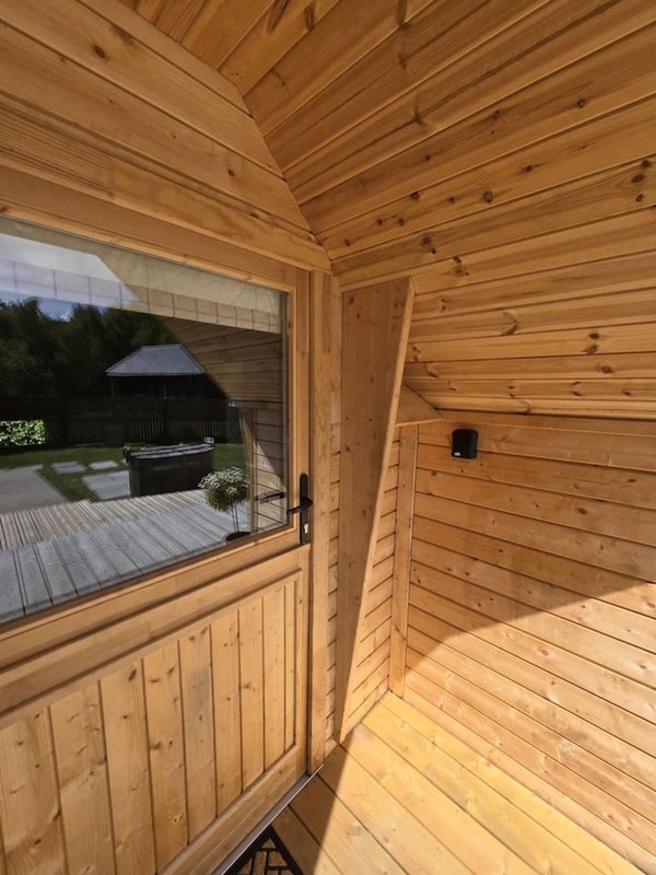 Interior of wooden cabin with glass door, wooden walls and ceiling, deck visible outside
