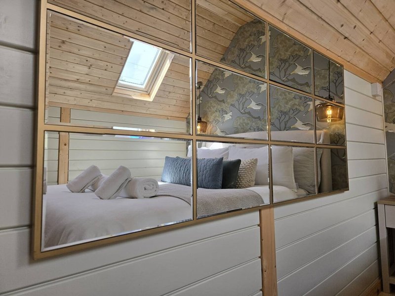 Bedroom with bed, decorative pillows, large mirror, wooden ceiling and skylight