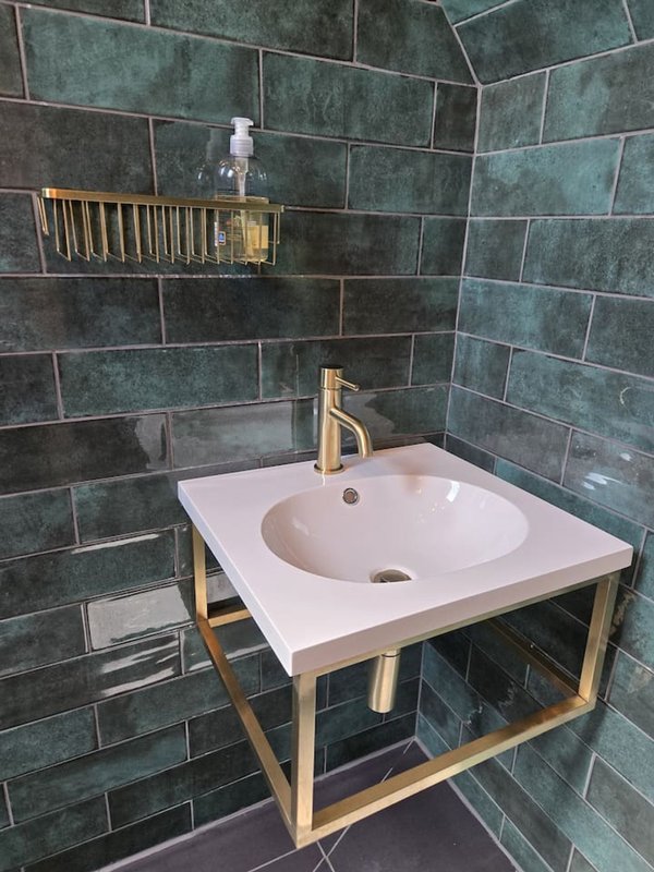 Modern bathroom with white sink, brass faucet, green tile walls and wooden frame vanity