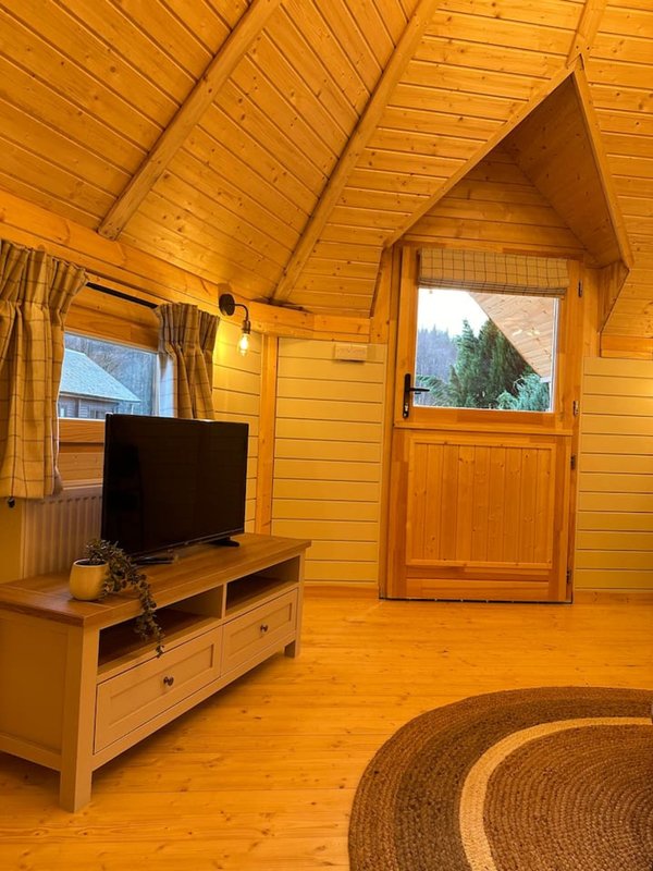 Wooden cabin interior with TV on stand, wooden furniture, and mountain view through door