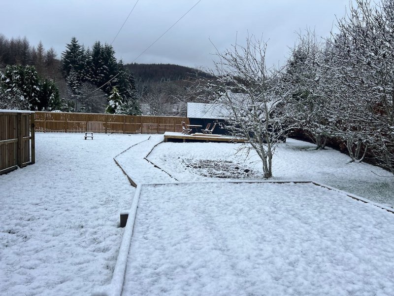 Snow-covered garden with wooden fence, bare trees, and distant hillside in winter