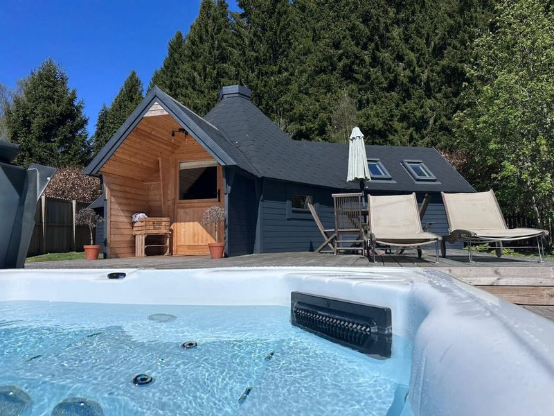 Modern accommodation with hot tub in foreground, wooden sauna, dark timber building and gardens