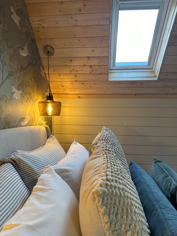 Cozy bedroom with wooden ceiling, skylight window, pendant lamp, and layered bedding with pillows