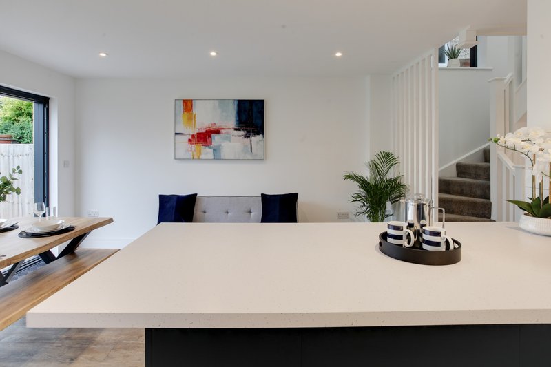Modern open-plan kitchen with white countertop, black island, and stairs visible in background