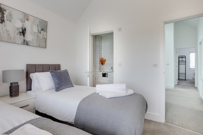 Bright modern bedroom with double bed, gray upholstered headboard, and ensuite bathroom visible through open door
