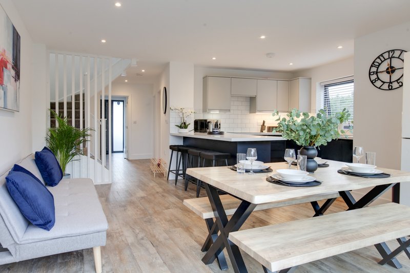 Open-plan kitchen and dining area with white sofa, wooden dining table and benches, black bar seating