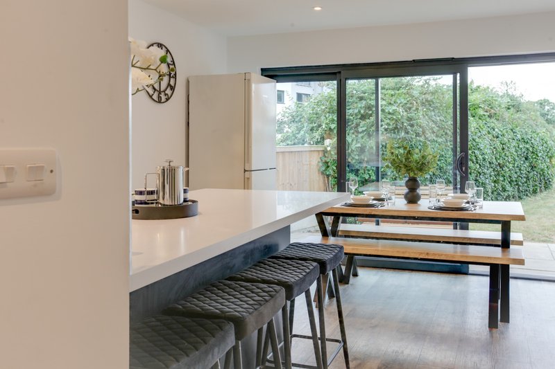 Modern kitchen with white countertop, bar seating, and dining table overlooking garden