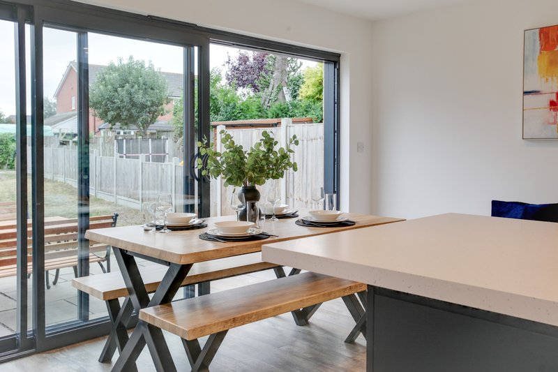 Modern dining area with wooden table, bench seating, and large glass doors opening to garden