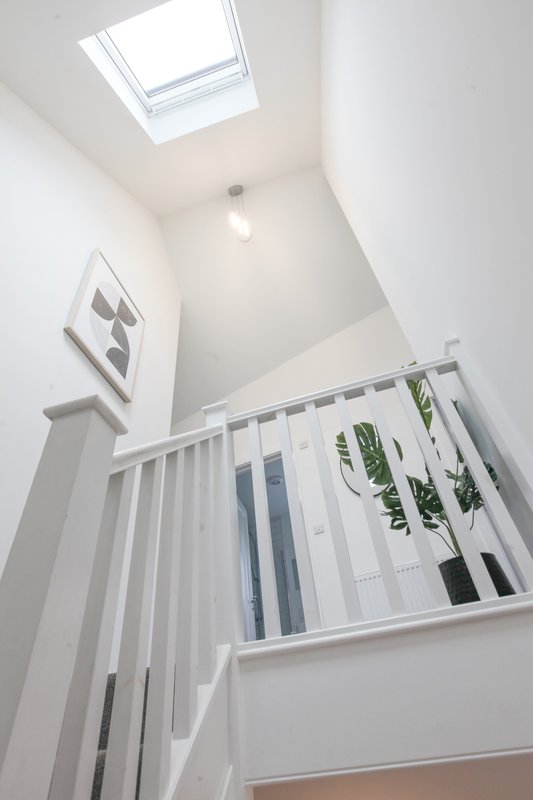 Bright stairwell with white railings, skylight, potted plant on landing