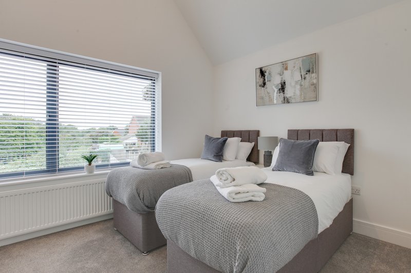 Modern bedroom with two double beds, grey bedding, large window and wall art