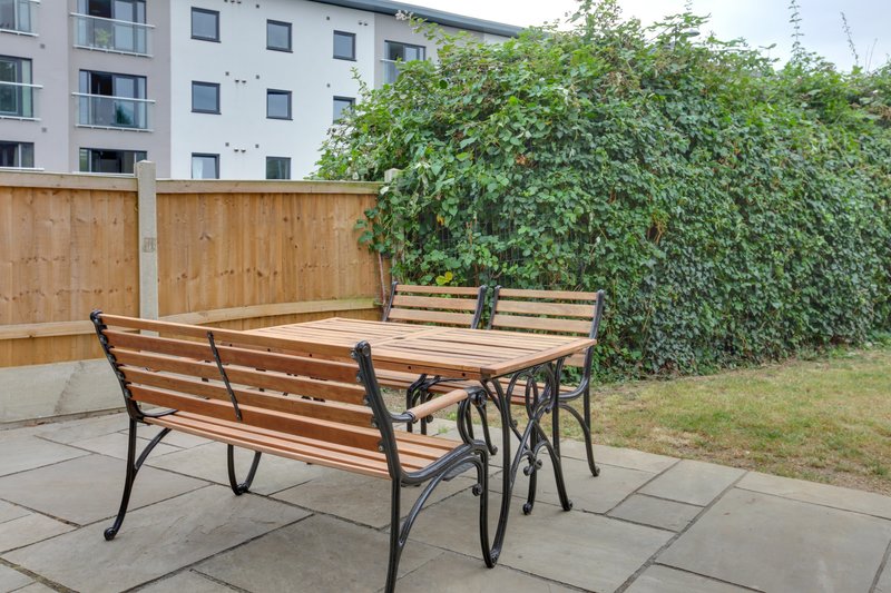 Communal garden patio with wooden benches, dining table, ivy-covered fence and apartment building
