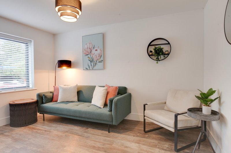 Bright living room with green sofa, cream armchair, wooden floor and modern lighting
