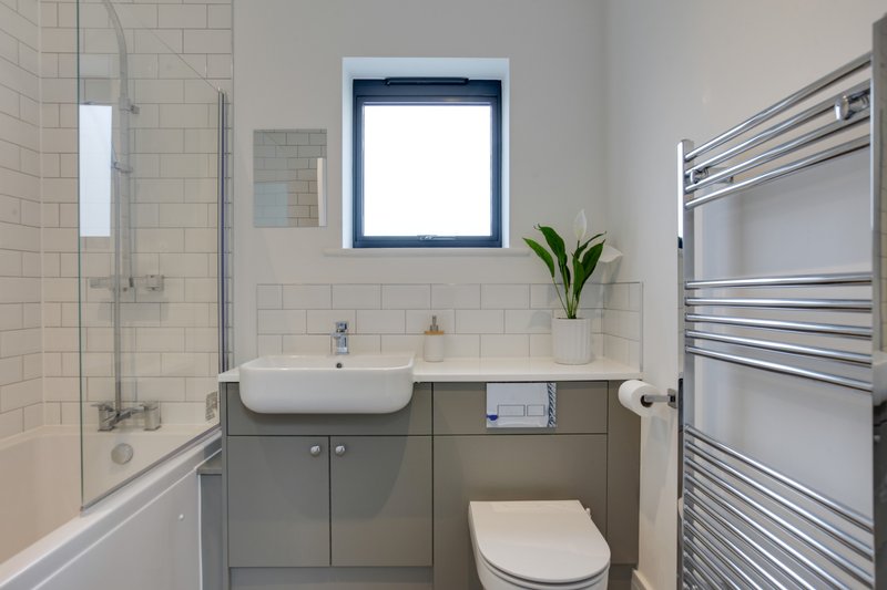 Modern bathroom with grey vanity, white sink, toilet, heated towel rail and shower enclosure