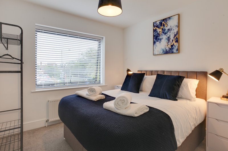 Modern bedroom with double bed, navy bedding, rolled towels, and window with blinds
