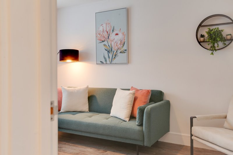 Modern living room with green sofa, decorative cushions, wall art, and pendant lamp