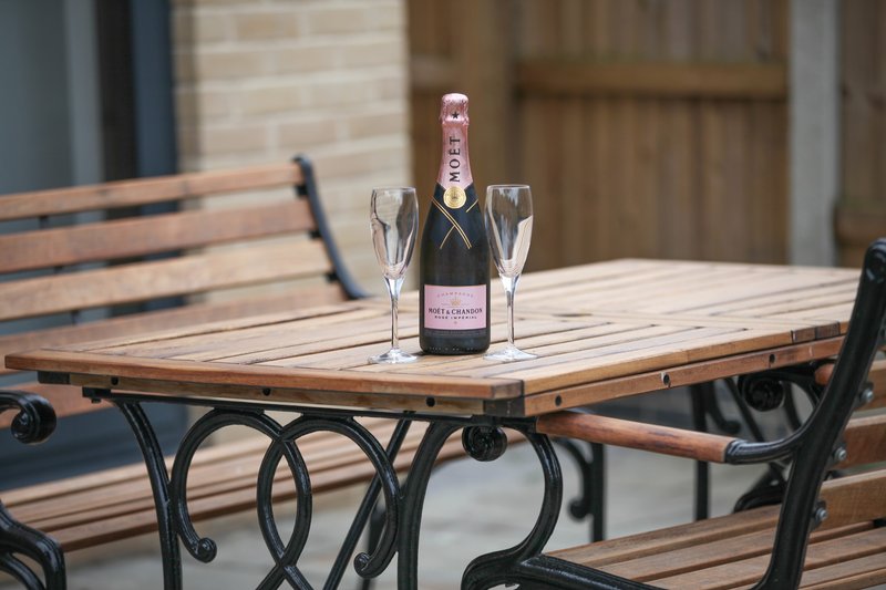 Outdoor dining table with champagne bottle and two glasses on wooden surface