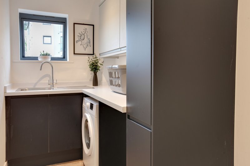 Modern utility room with washing machine, sink, window and dark cabinetry