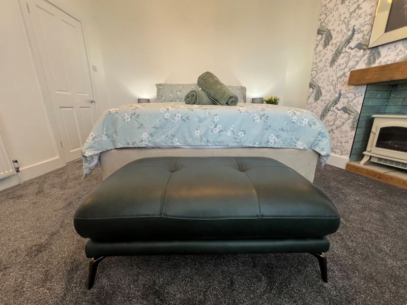 Bedroom with double bed, black ottoman bench, rolled towels, and fireplace