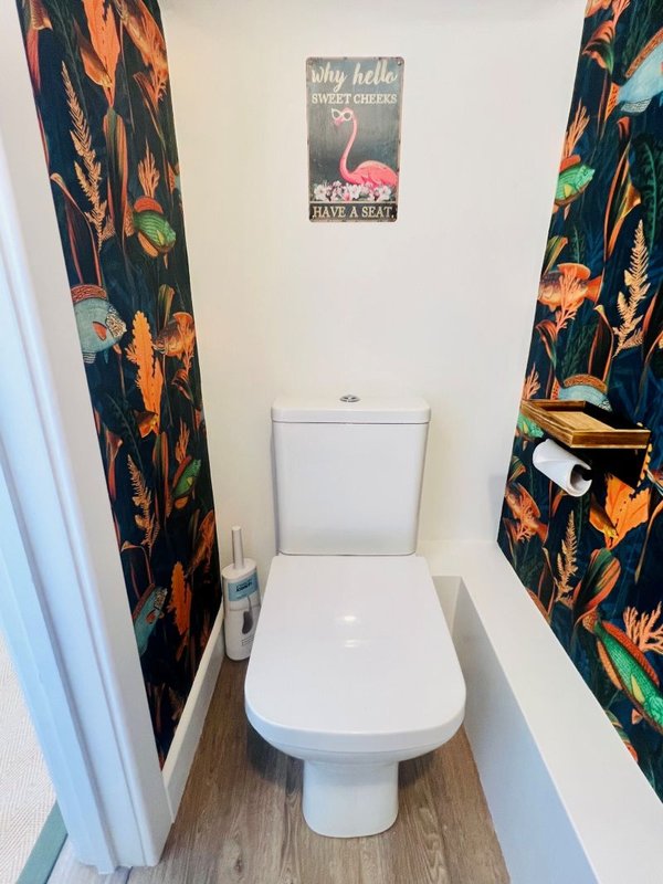 Compact bathroom with white toilet, colorful patterned curtains and decorative wall sign