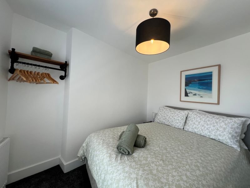 Modern bedroom with double bed, black ceiling lamp, framed beach artwork, and wall shelf