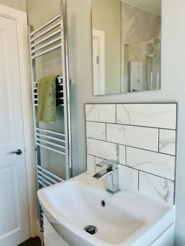 Modern bathroom with white sink, chrome tap, heated towel rail and marble tile splashback