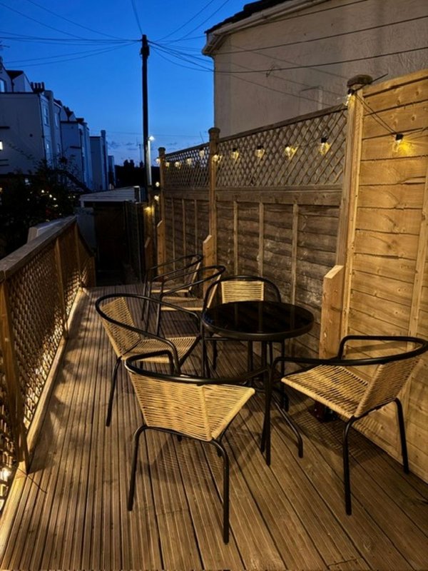 Rooftop terrace with wooden decking, metal table, chairs, and lattice fence panels