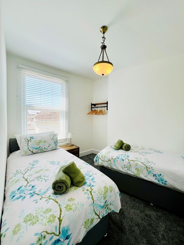 Bright bedroom with two single beds, floral bedding, pendant light, and window with blinds