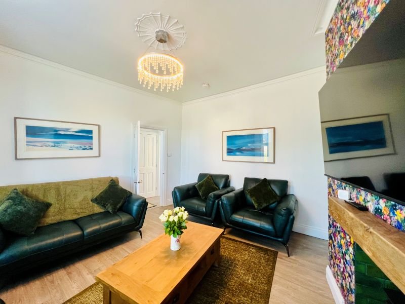 Modern living room with green leather sofas, wooden coffee table, ceiling pendant light and framed artwork