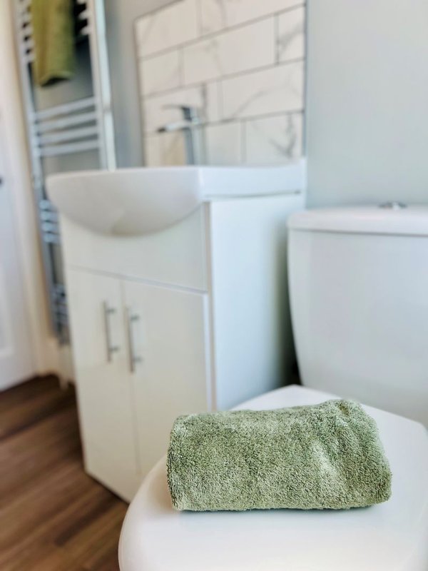 Modern bathroom with white vanity sink, toilet, and folded green towel on lid
