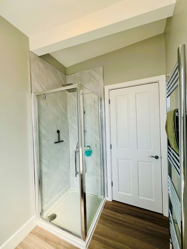 Modern bathroom with walk-in shower, marble tile surround, heated towel rail and white door