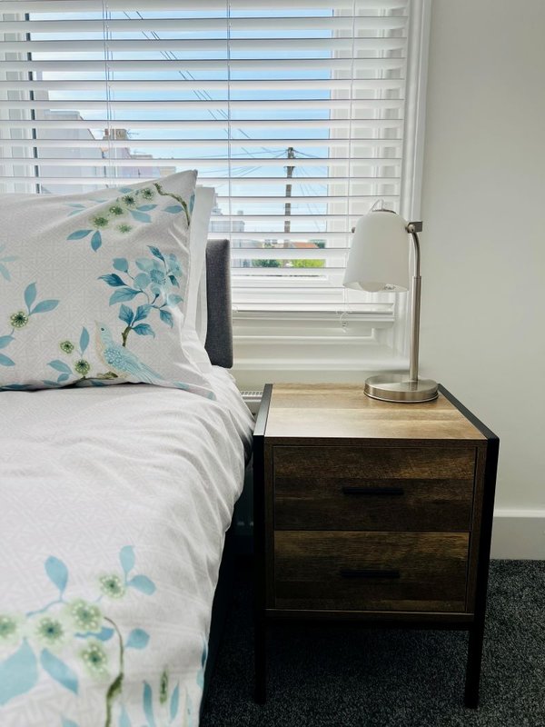 Bedroom with double bed, patterned pillows, dark wood nightstand, and window with blinds