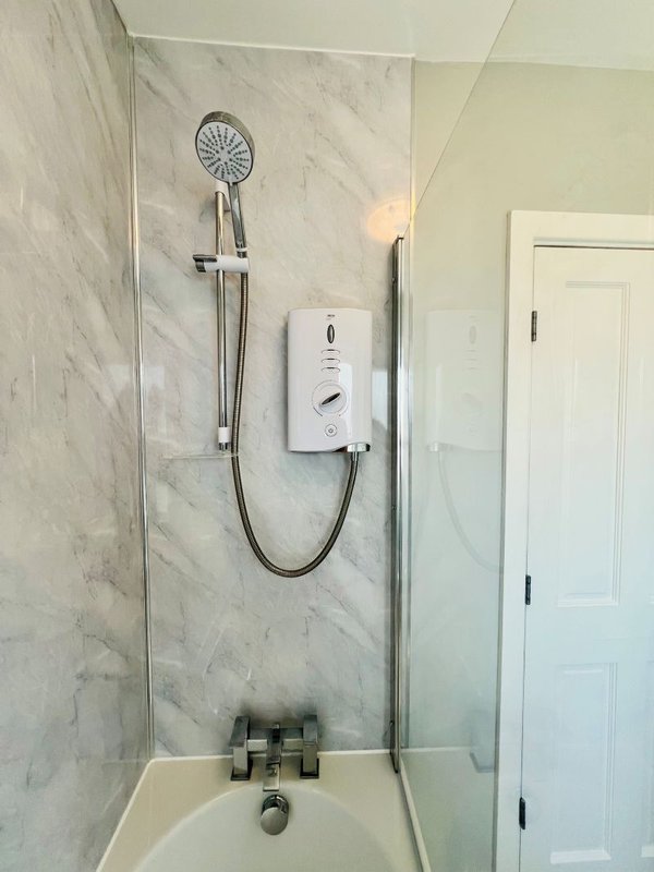 Bathroom shower enclosure with marble tiles, rainfall showerhead and white electric heating unit