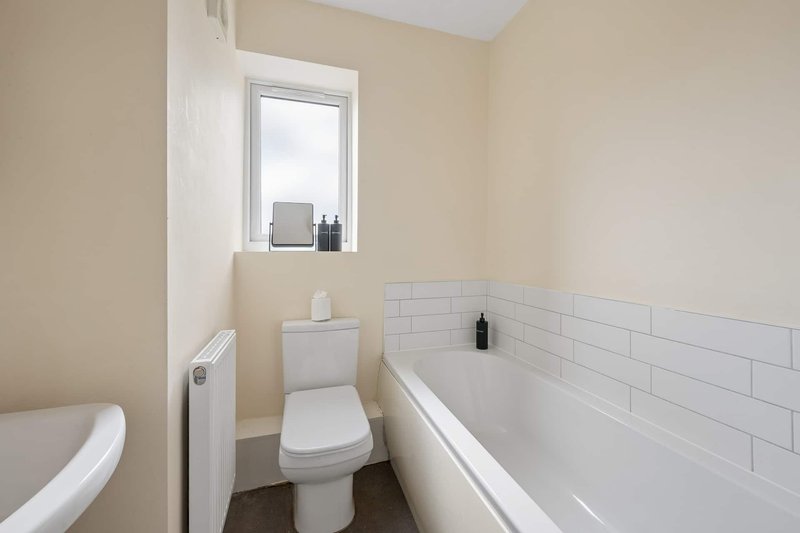 Small bathroom with white toilet, bathtub, subway tile wall and window