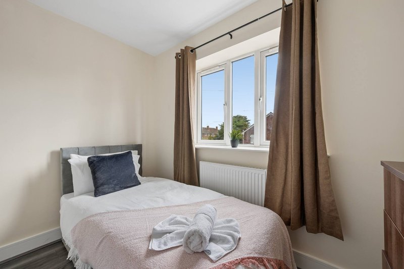 Bedroom with single bed, window with brown curtains, radiator and neutral walls