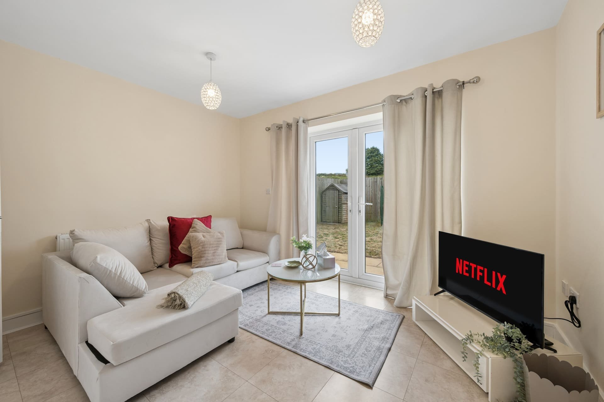 Bright living room with cream sofa, pendant lights, TV, and glass doors opening to garden