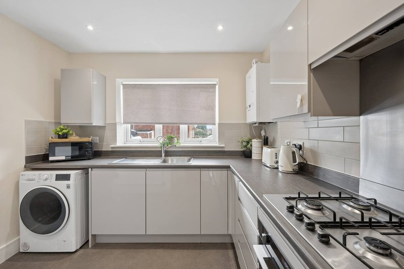 Modern kitchen with white cabinetry, gas range, washing machine, and window with blind