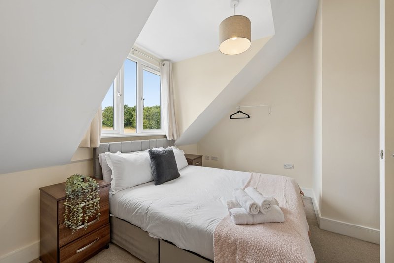 Small bedroom with single bed, wooden bedside table, sloped ceiling and window with garden view