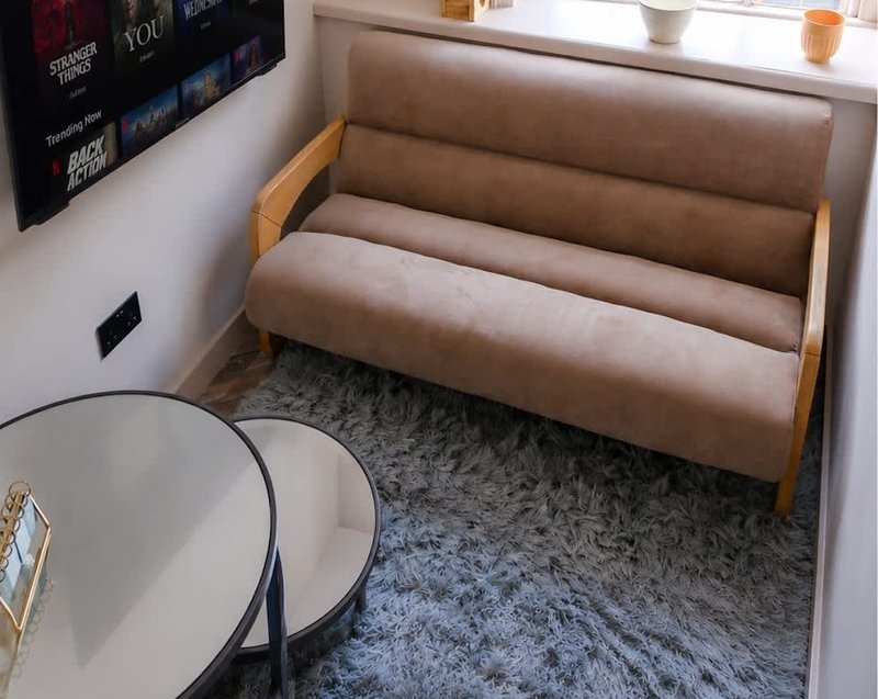 Compact living room with beige sofa, round white table, and grey rug