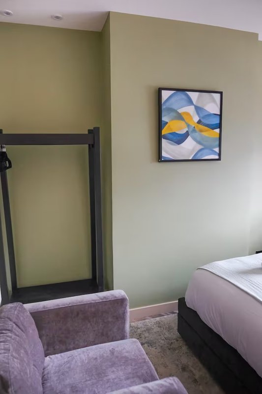 Bedroom with double bed, purple armchair, framed abstract artwork and black-framed door